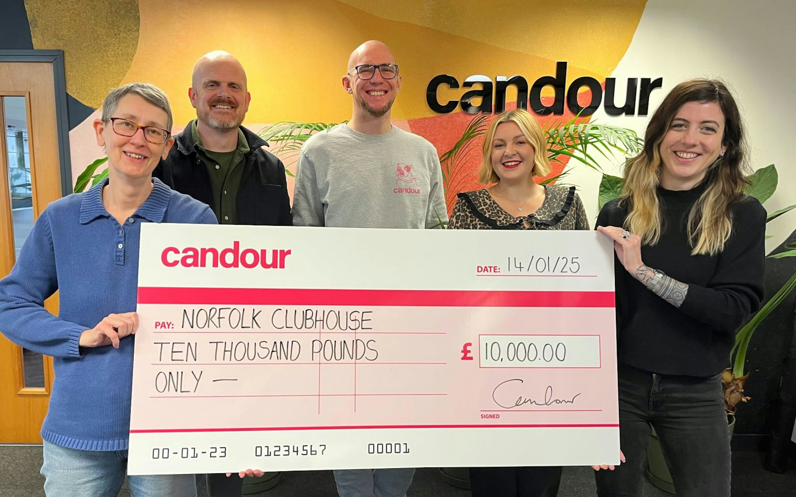 Five people in the Candour offices holding up a large comedy-sized cheque from Candour to Norfolk Clubhouse for £10000. From left to right (all smiling gratuitously): June Web, John Skinner, Mark Williams-Cook, Jessica Bettis and Tabby Farrar