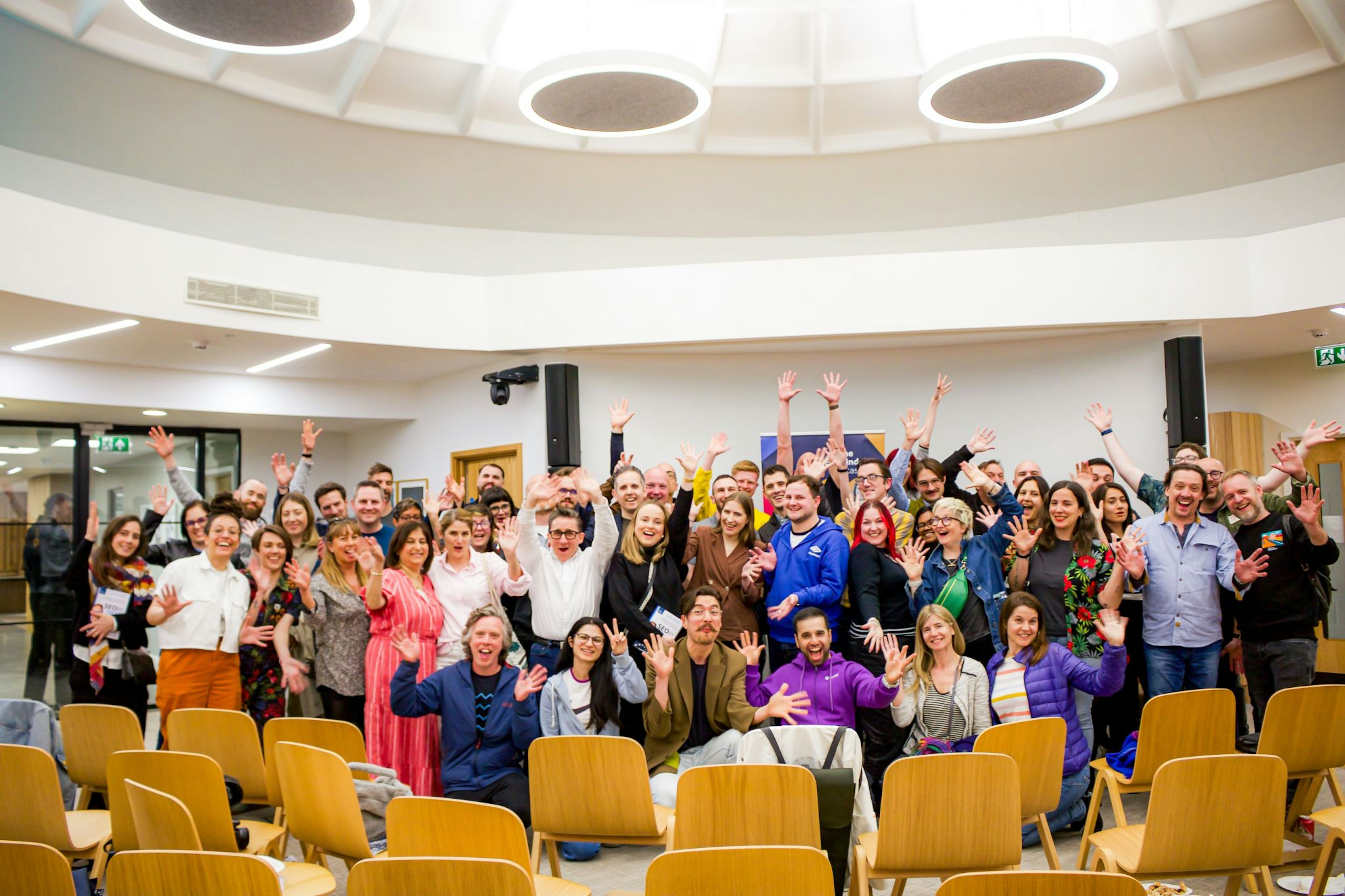 A large group of attendees to the Live podcast facing the camera while smiling and waving jazz hands