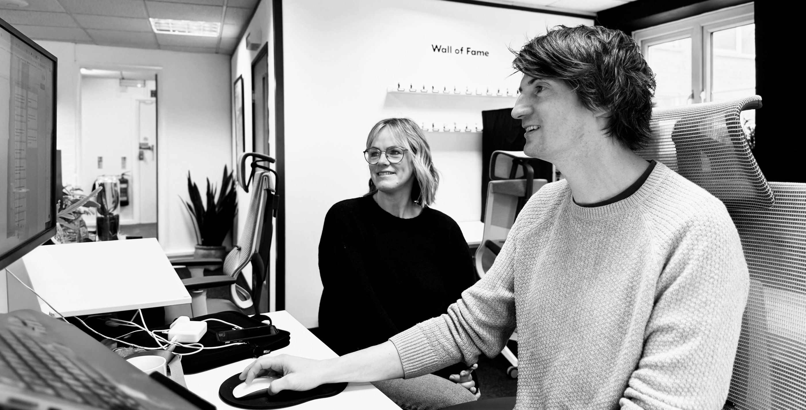Annette Ireson and Mark Salisbury sitting together at a desk discussing something they are looking at on the computer screen in front of them in a light and airy office