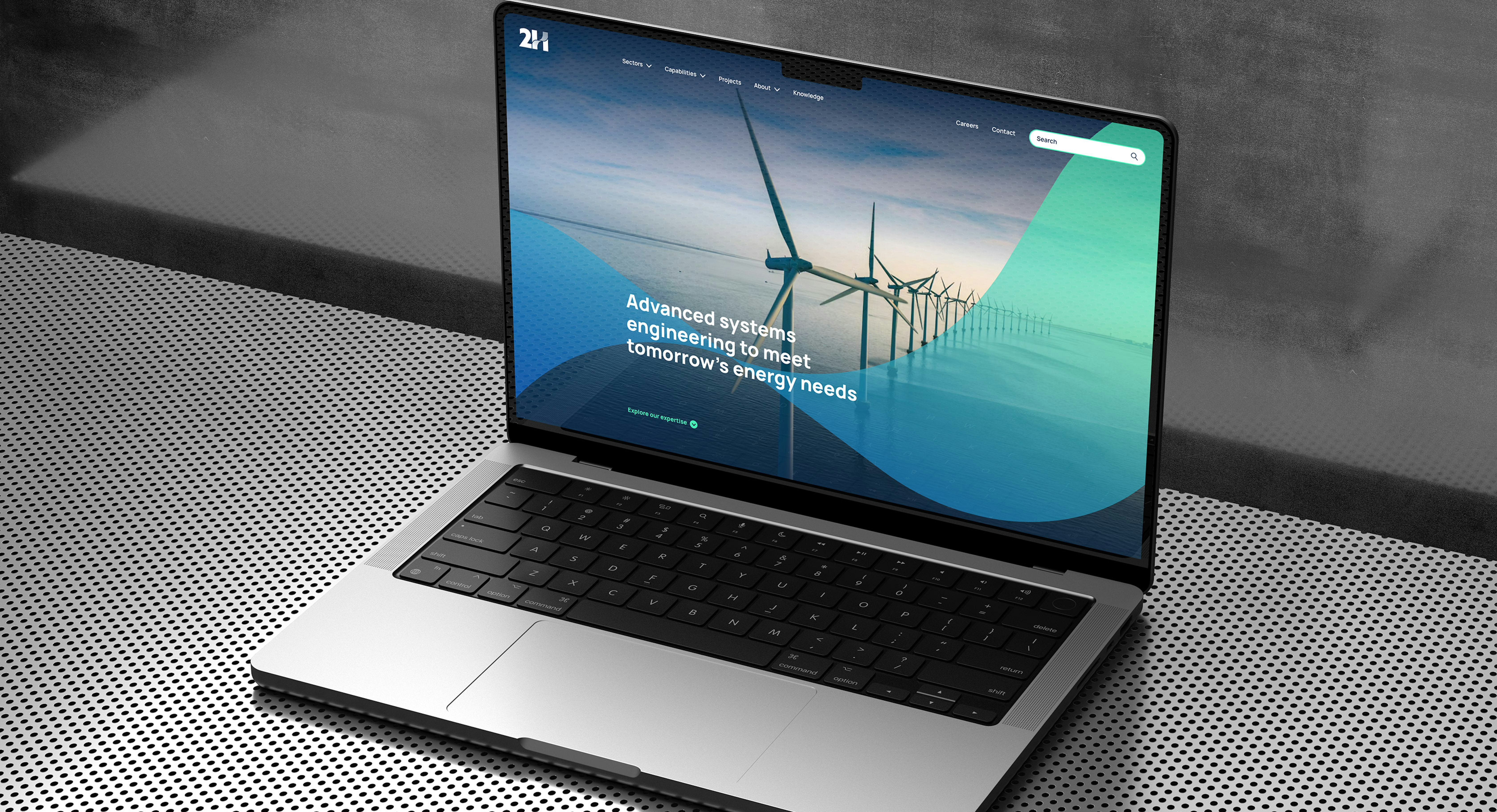 An open laptop computer on a metal surface display the hero section of the 2H website homepage