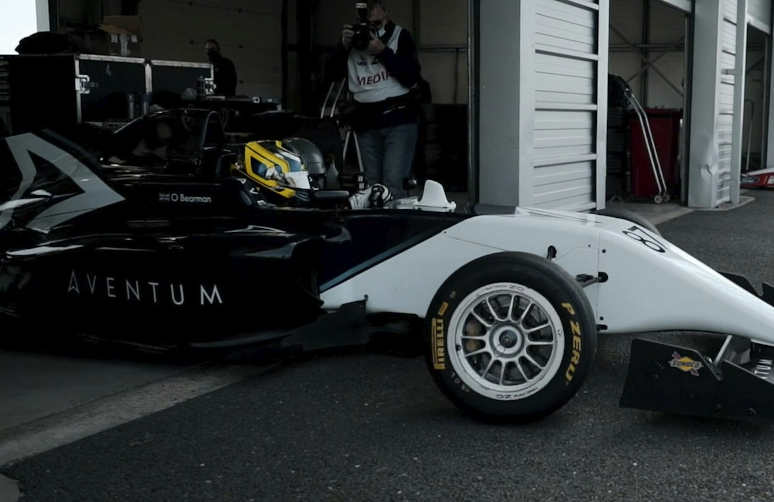 A side view of a racing car as it exits a pit garage, it is displaying the Aventum logo on a side panel