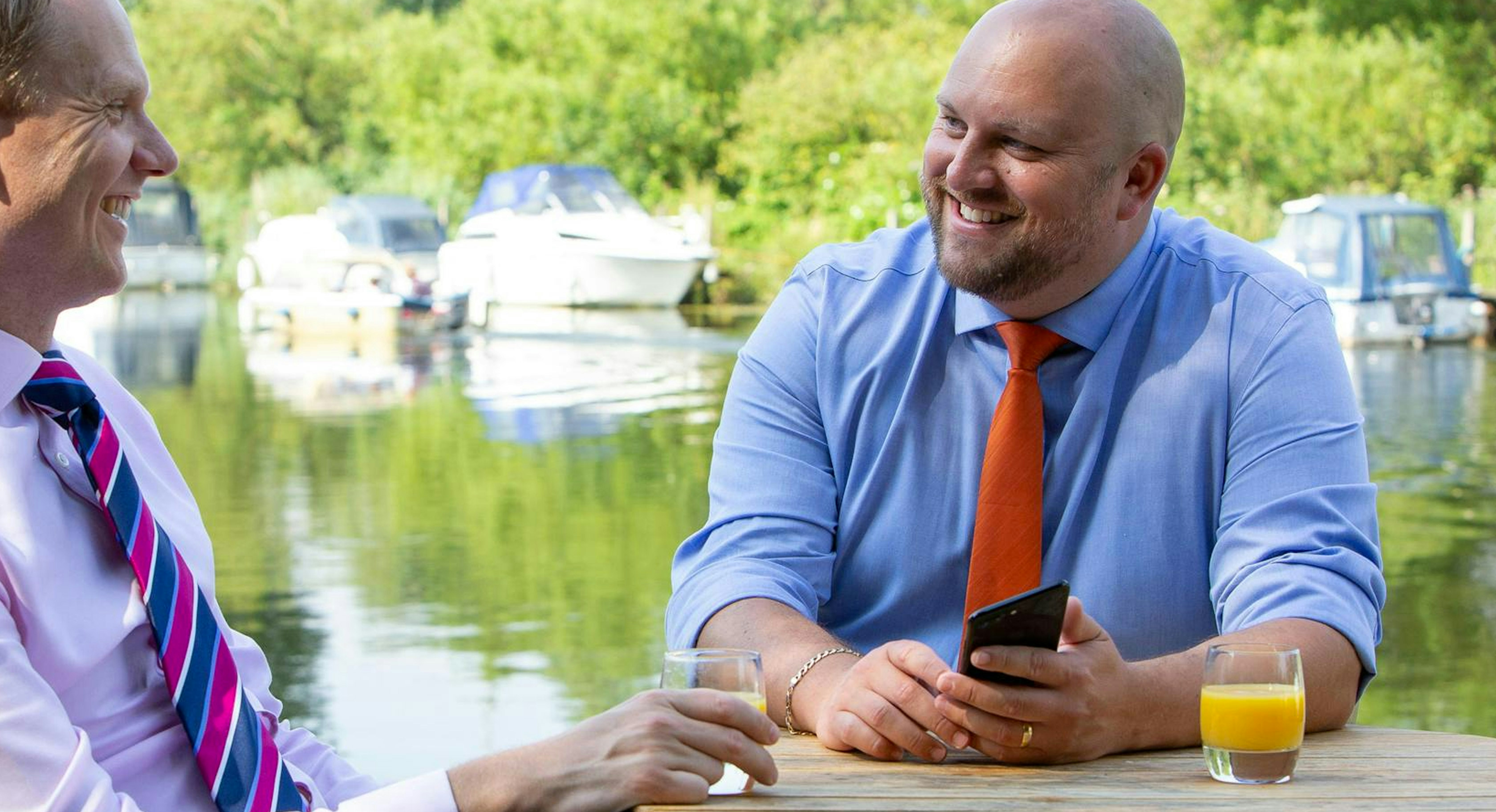 Two accountants from Lovewell Blake talking while enjoying a soft drink at a table next to a river