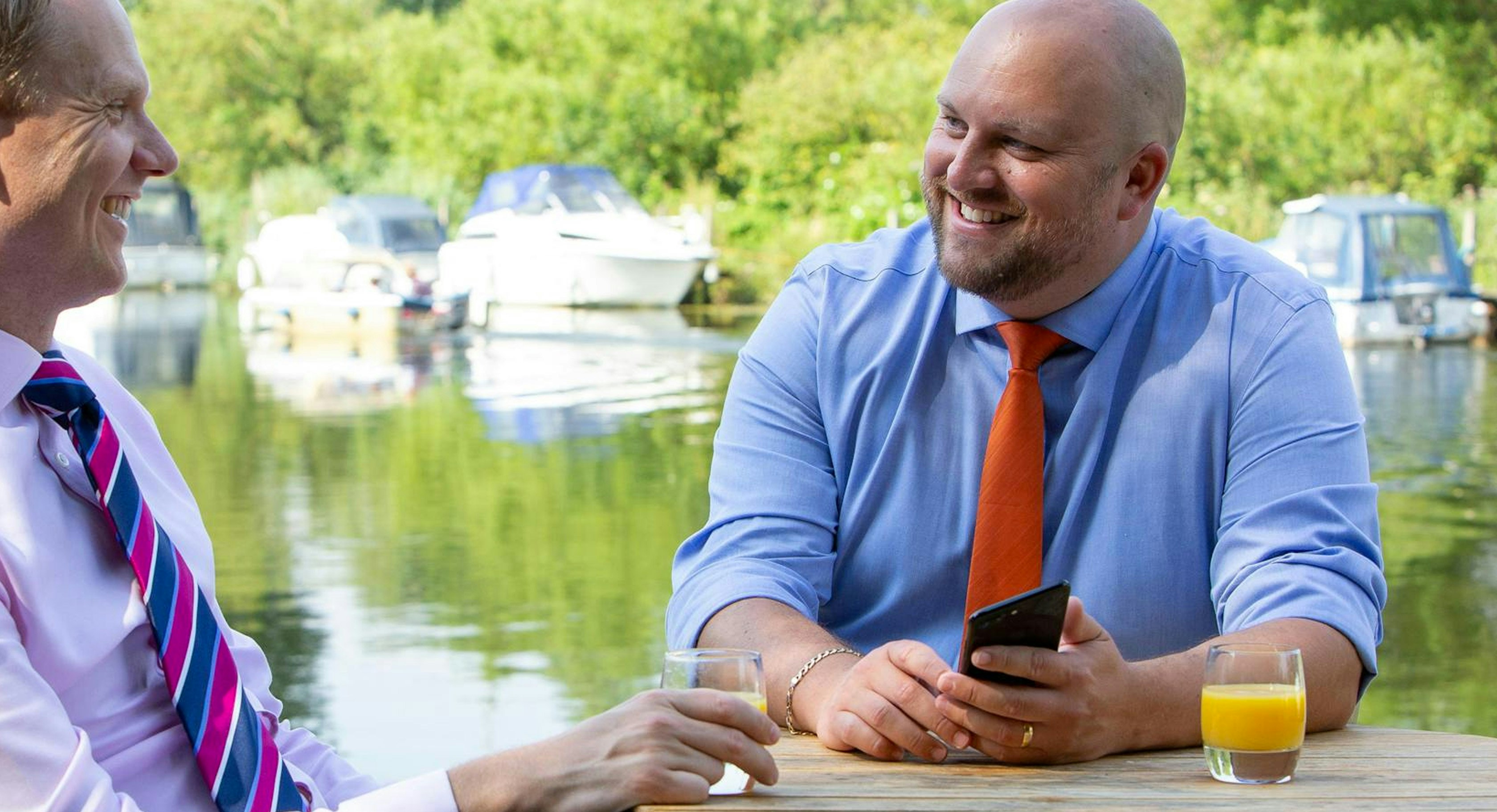 Two accountants from Lovewell Blake talking while enjoying a soft drink at a table next to a river