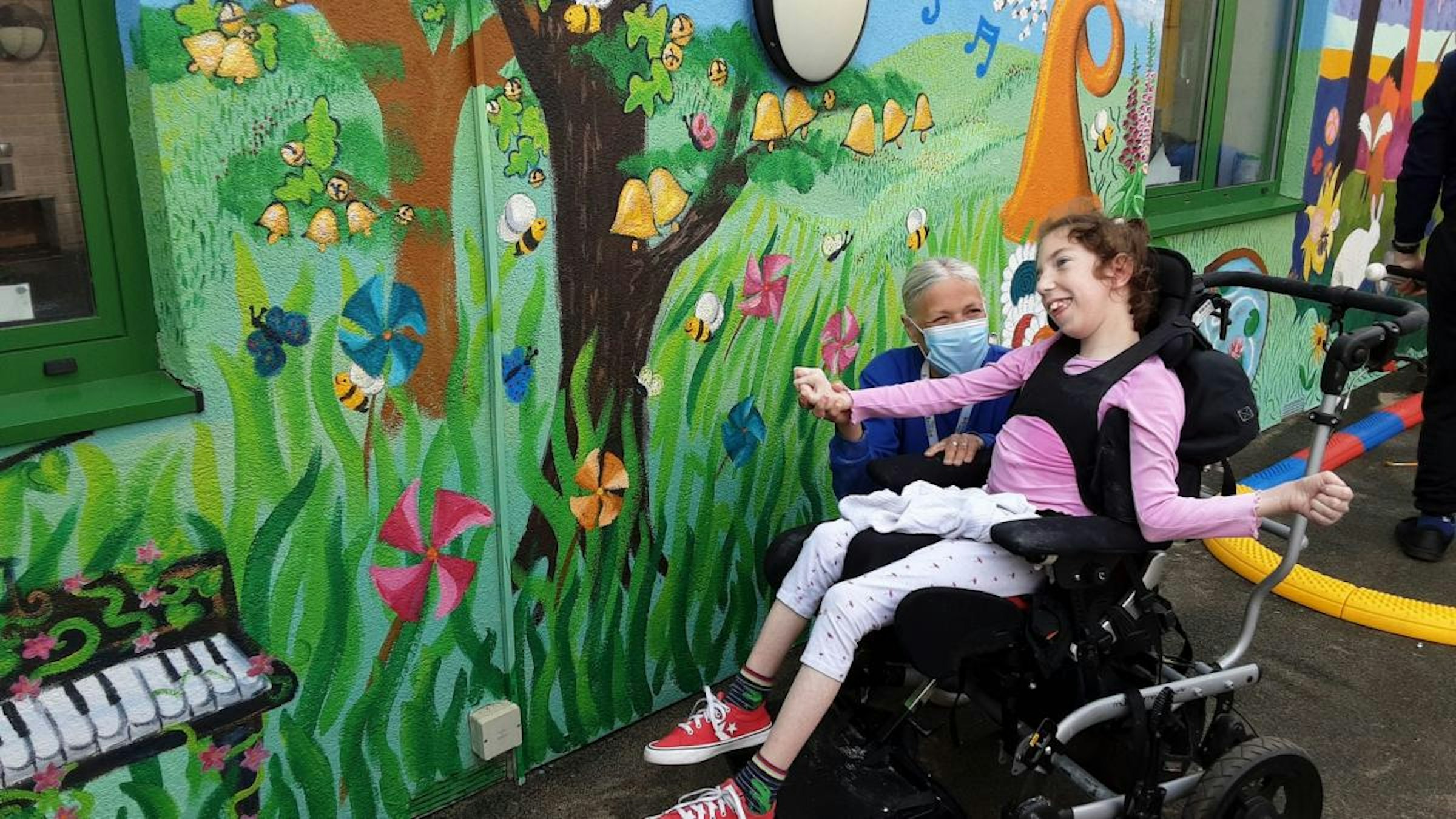 A photo of a service user and a support worker next to a colourful mural at the Hamlet Charity in Norwich