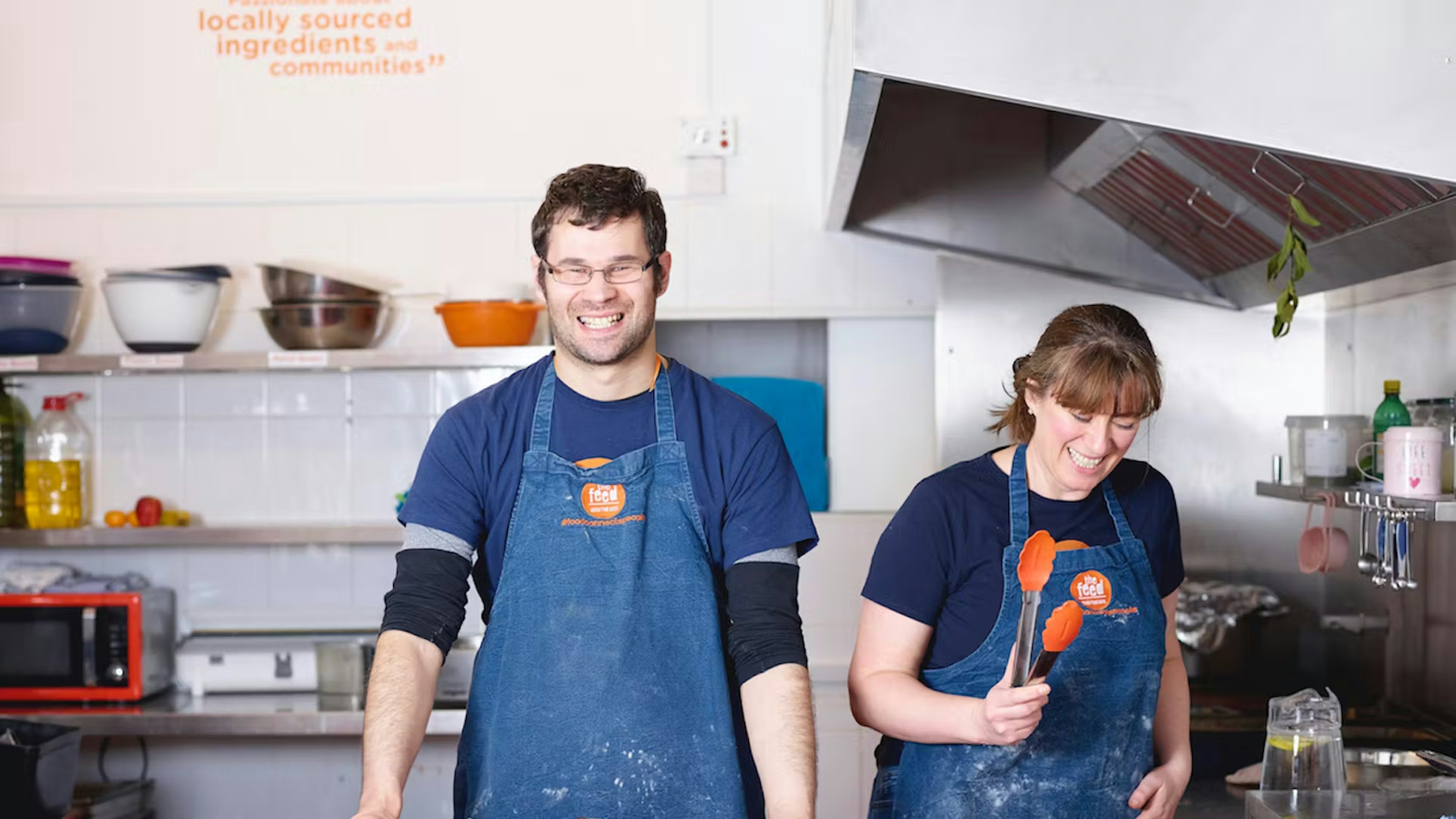 A man and woman smiling while working in a kitchen at The Feed