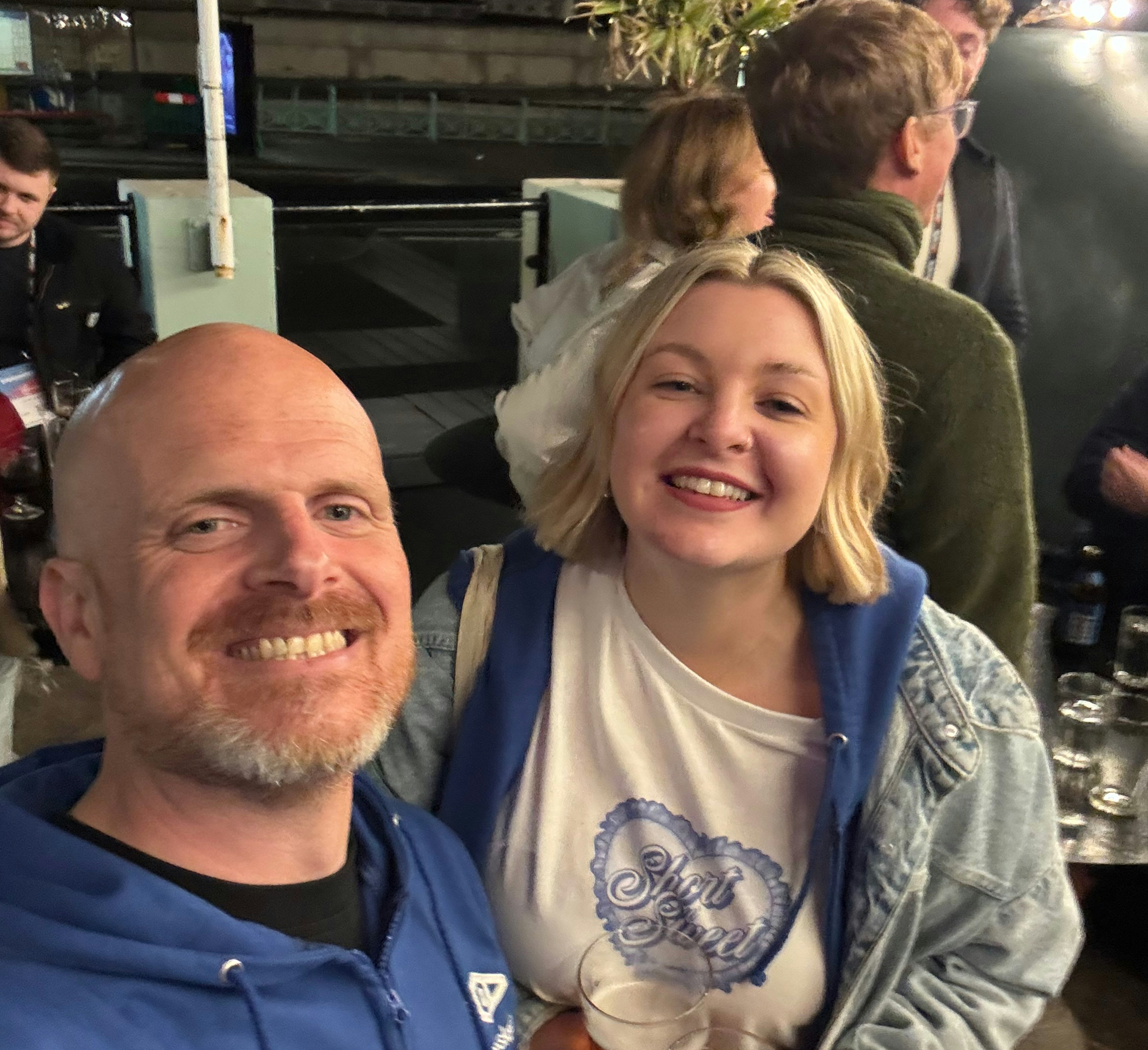 John Skinner and Jessica Bettis smiling gormlessly at the camera at a BrightonSEO after party. They may have had a drink.
