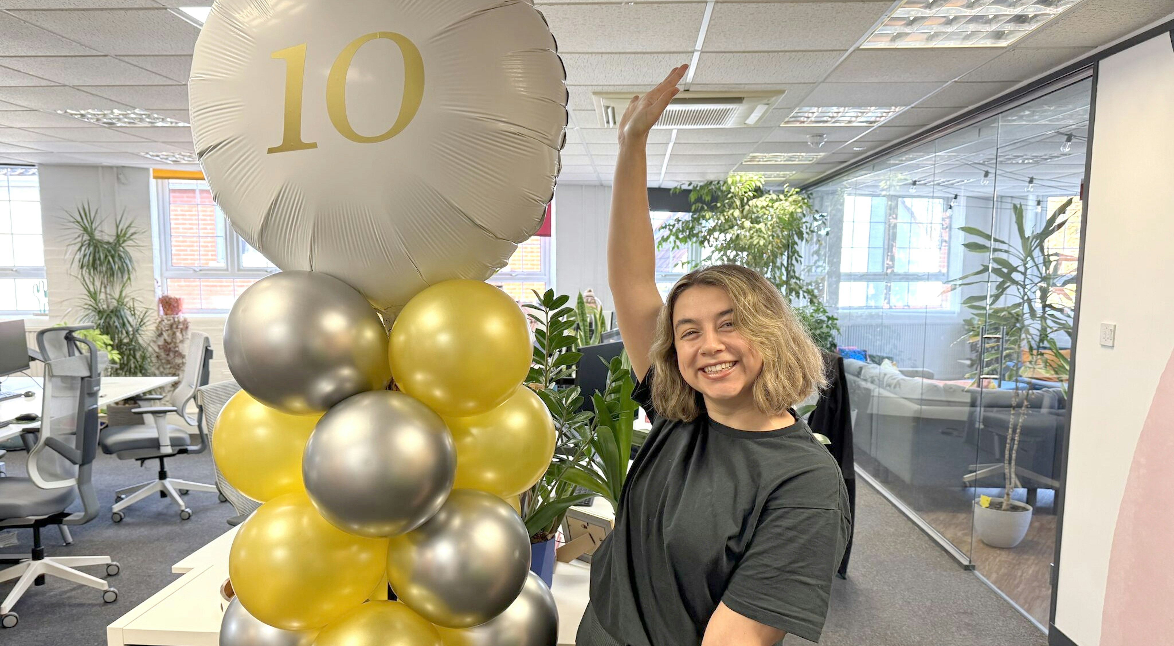India Bobby (with a beaming smile) standing next to a balloon tower made up of many silver and gold coloured balloons. The one at the top has the number 10 on it.