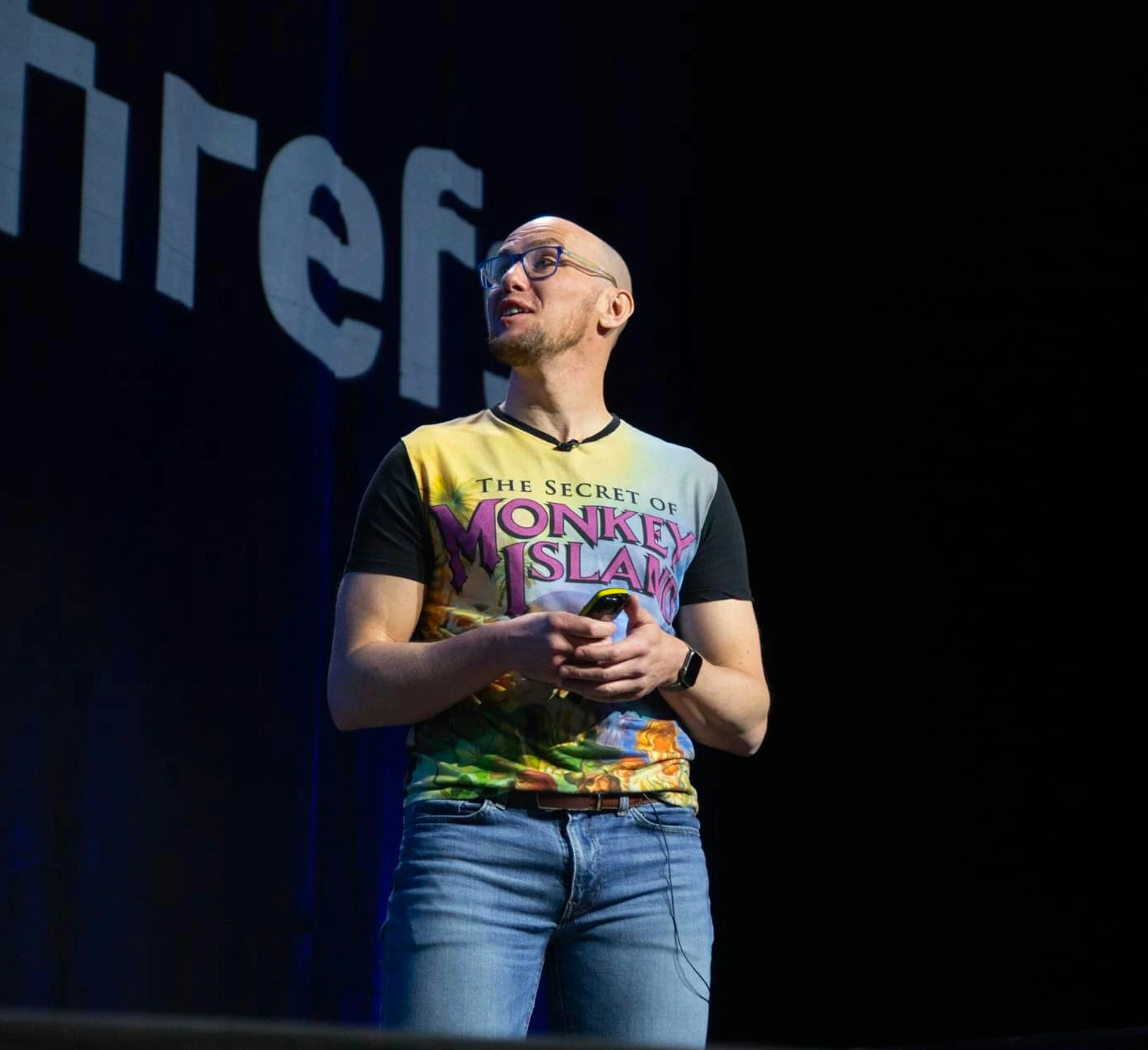 Mark Williams-Cook in the spotlight on stage at BrightonSEO. He is wearing a Monkey Island t-shirt even though it isn't 1995.