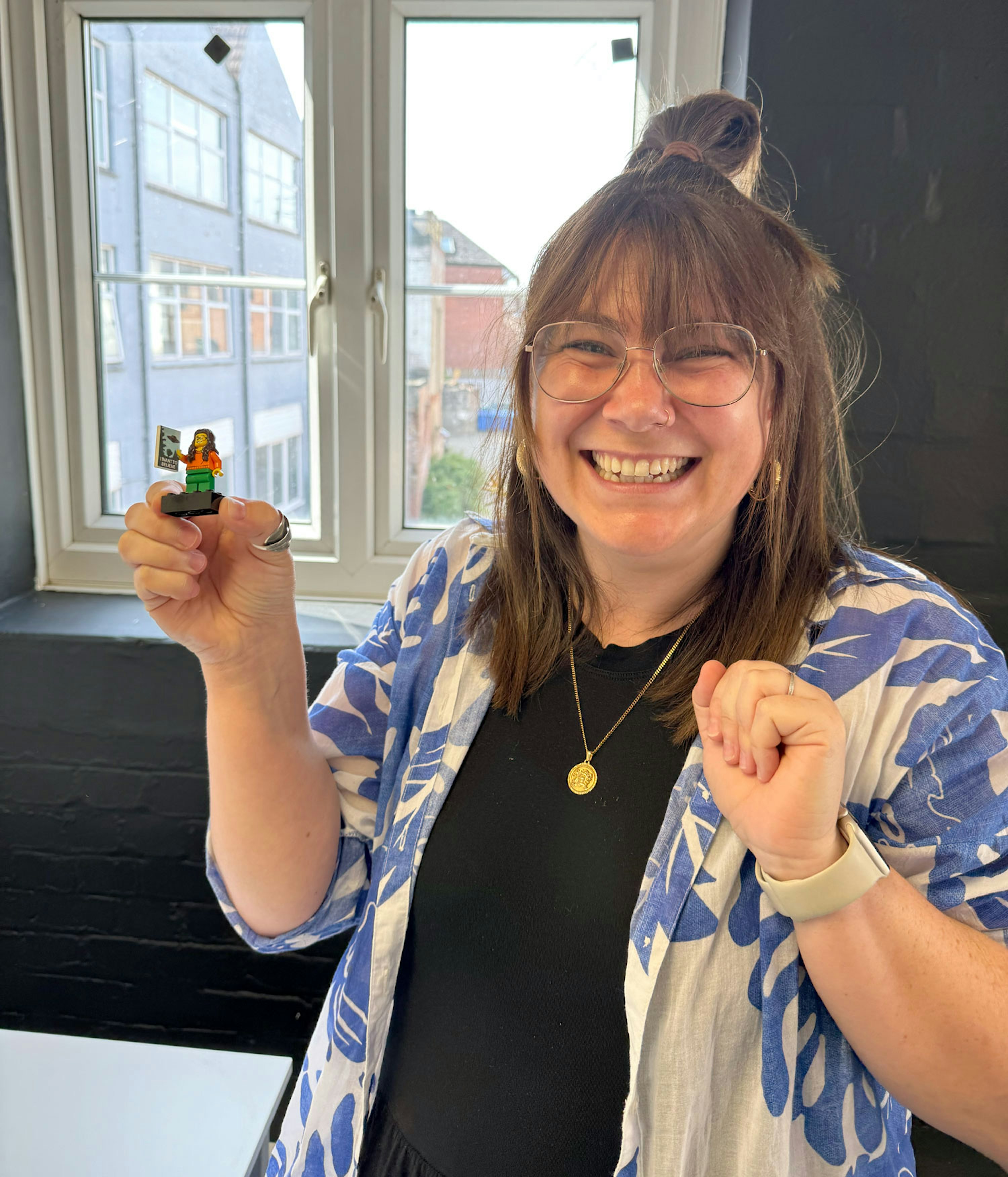 Sammy Marshall smiling (perhaps even beaming) at the camera while holding up a lego minifigure of herself