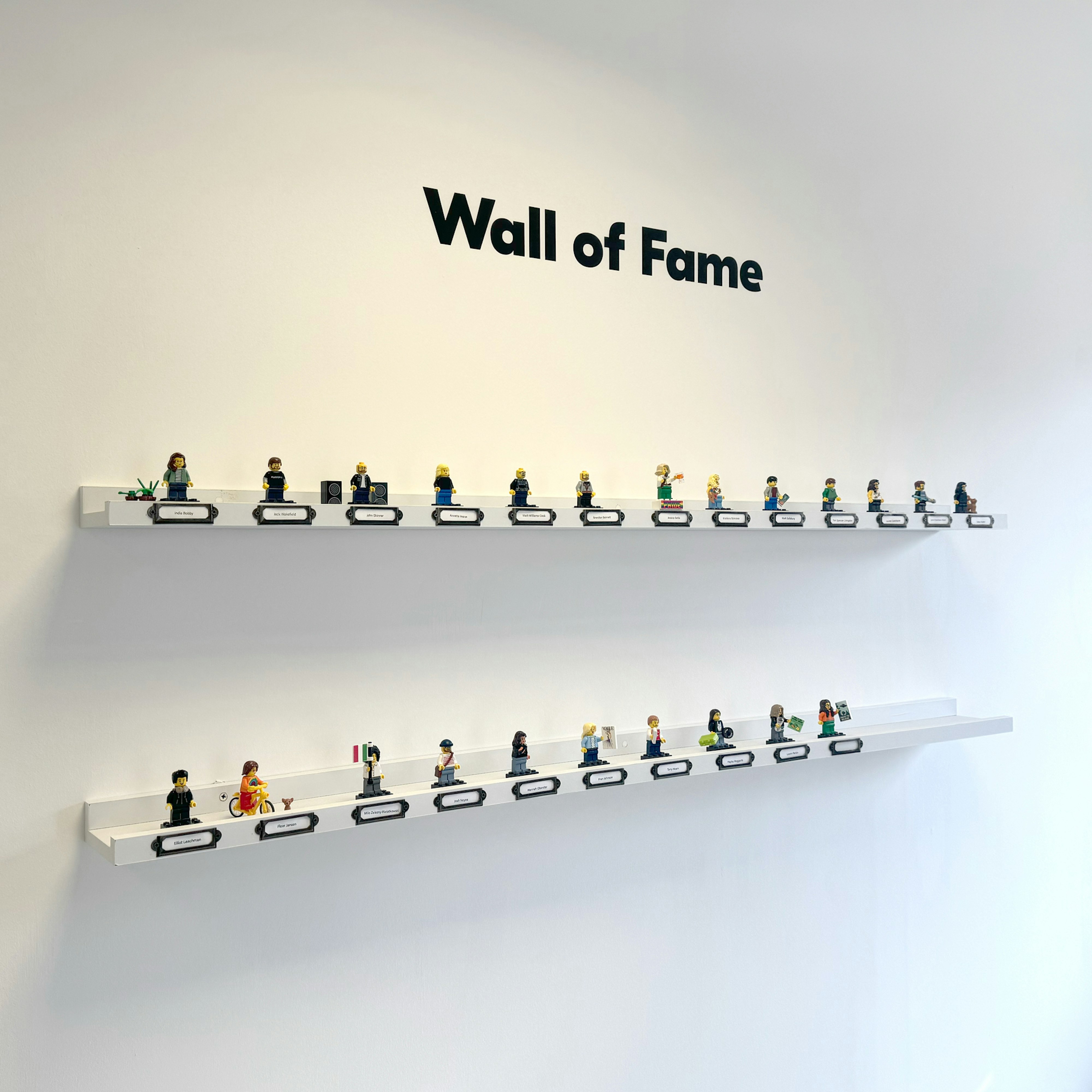 a white wall with two long shallow white shelves, displaying 23 lego minifigures of the Candour Team. The words 'Wall of Fame' appear above the shelves on the wall in bold black lettering.