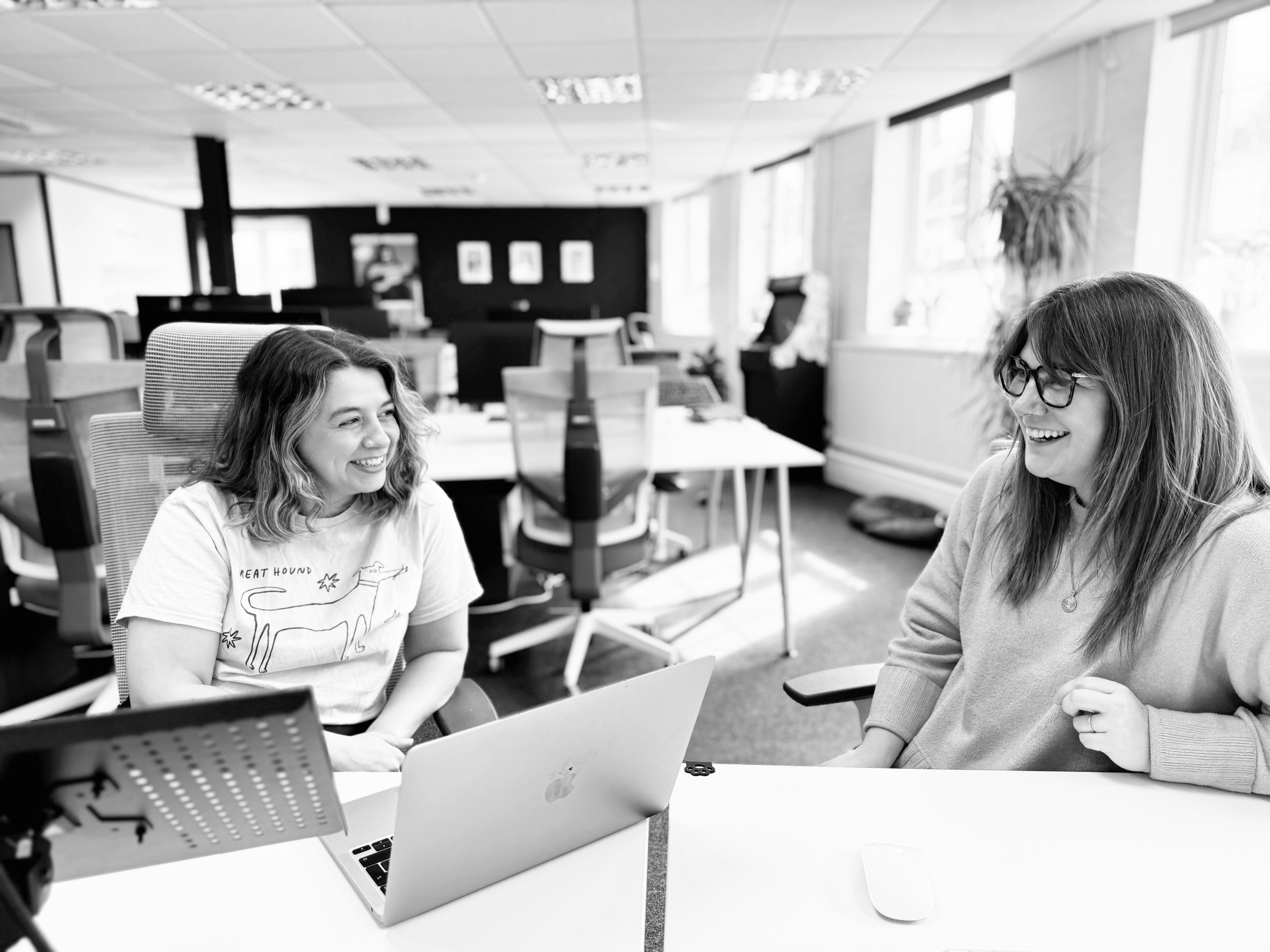 Two women, India Bobby and Sammy Marshall are sitting together at a desk in the sunny Candour office, smiling while in conversation with eachother.