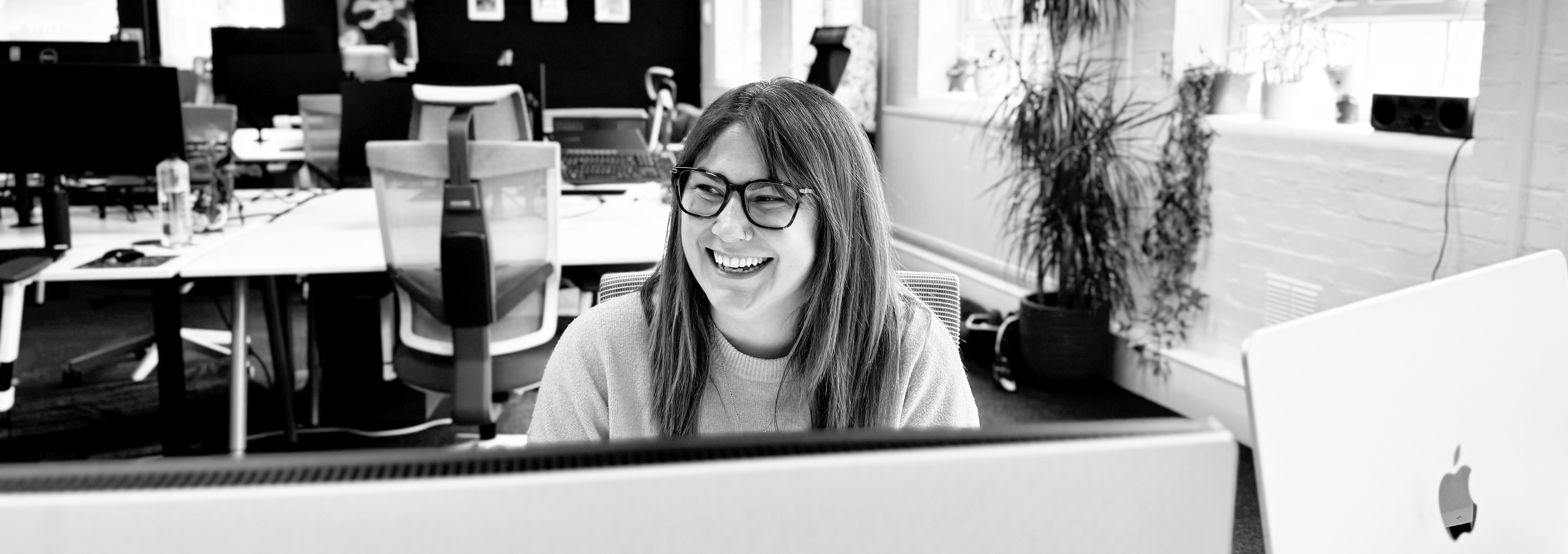 Sammy Willets, our senior account manager sitting at her desk in a sunlit office, smiling (as always)