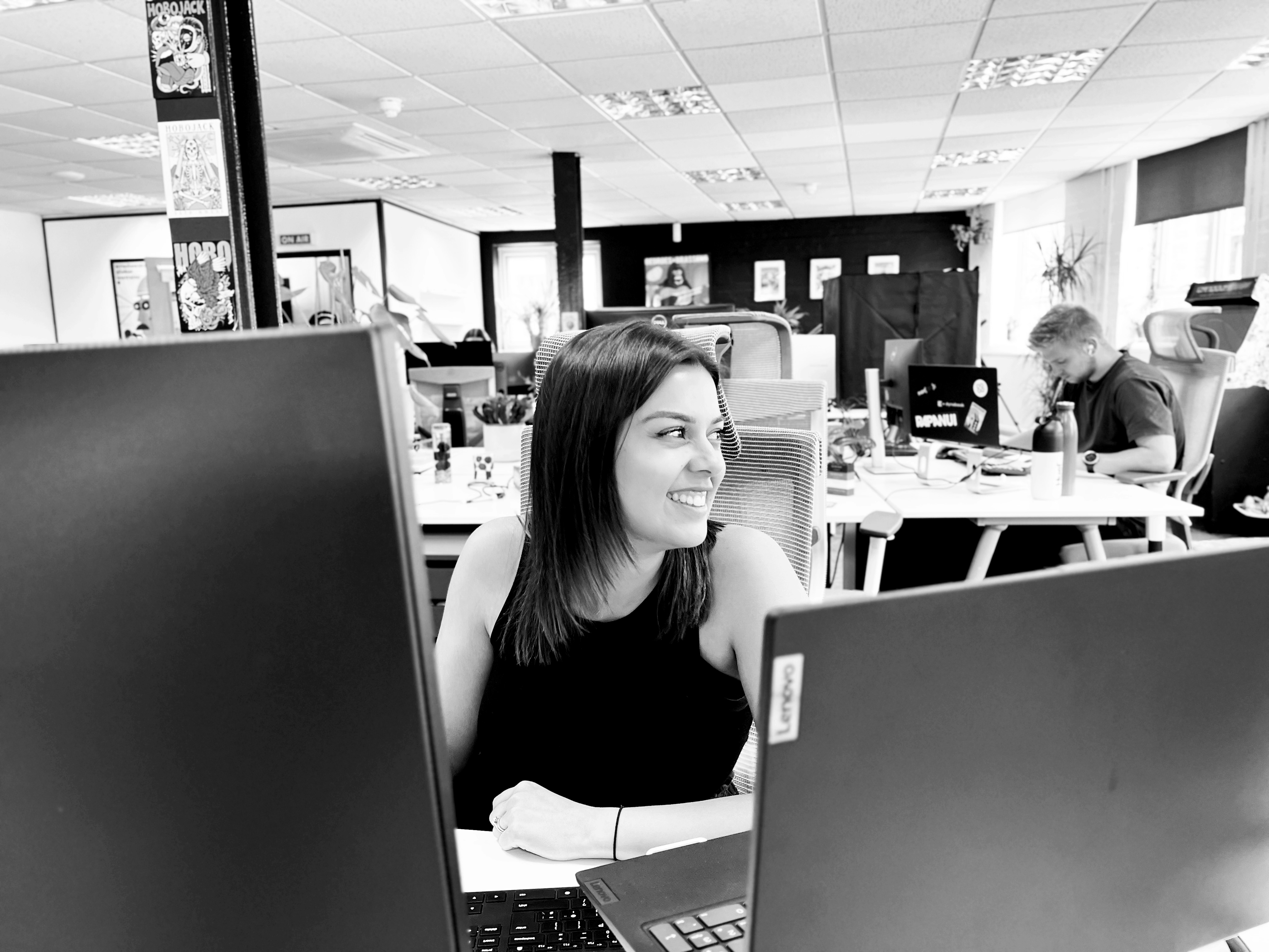 A team member at Candour, sitting at her desk and smiling at a colleague (out of shot).