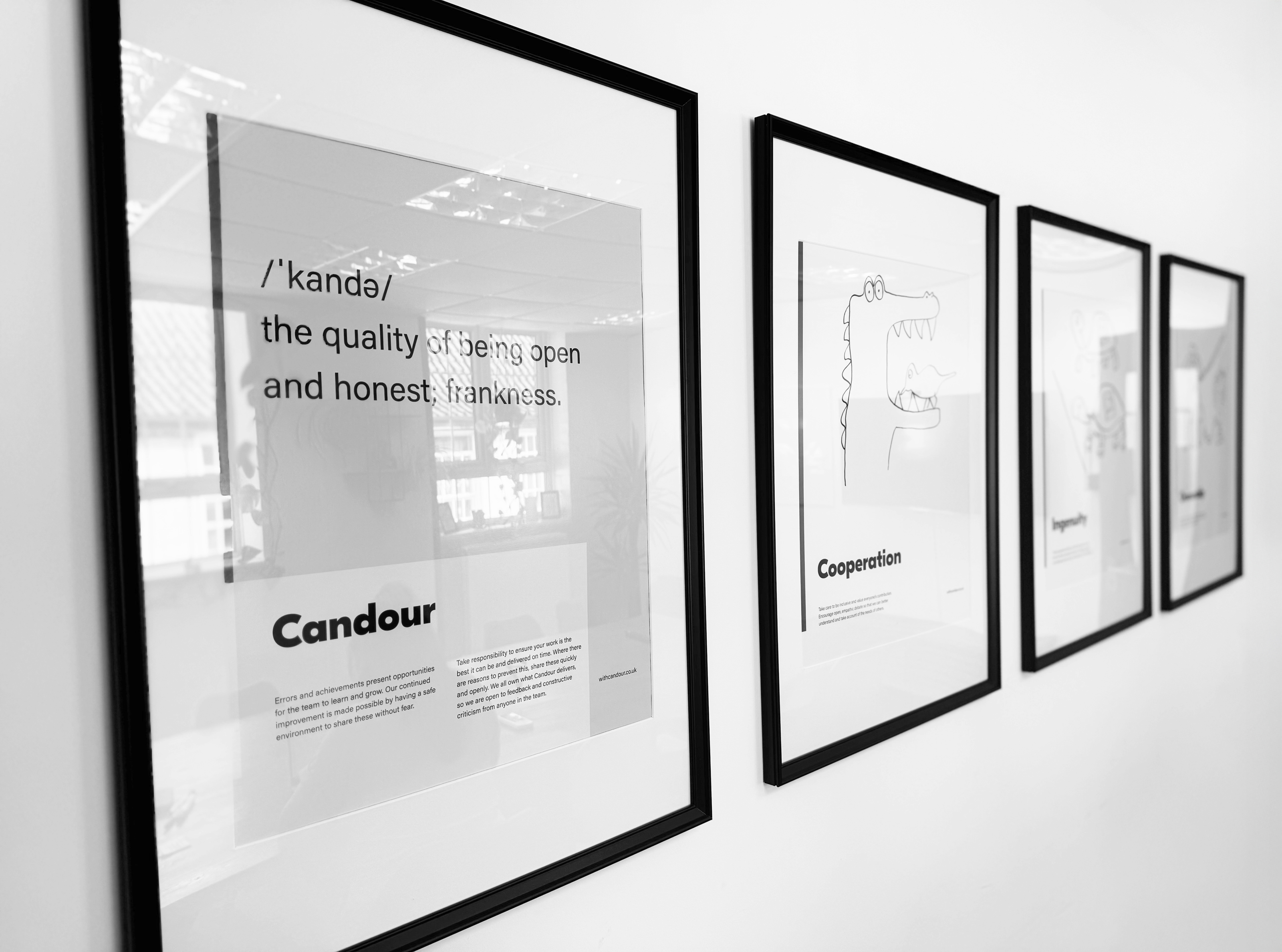 four framed posters on a white wall. The first poster has the value of 'Candour' displayed with the defiition of that word, the second 'Cooperation', with and illustration of a crocodile having eats teeth cleaned by a bird. The other two are out of focus.