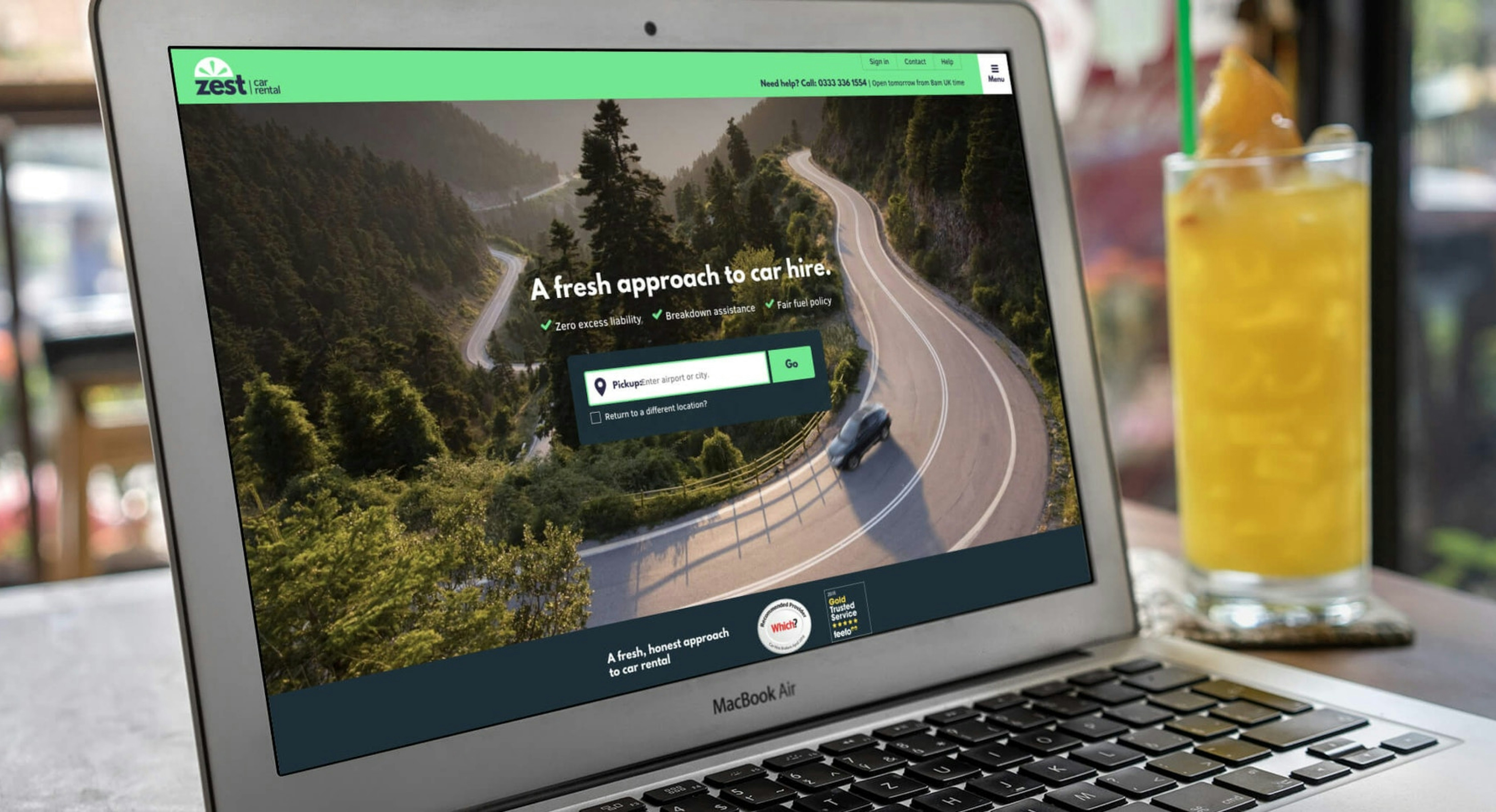 A MacBook Air displaying the Zest Car Rental website, featuring a scenic winding road, a search bar for car hire, and a fresh approach to rental services.
